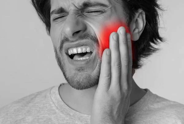 man holding his left cheeks while in pain from the toothache